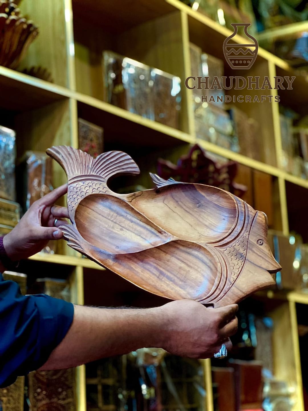 Wooden fish-shaped platter held by a person with a blurred background of shelves.